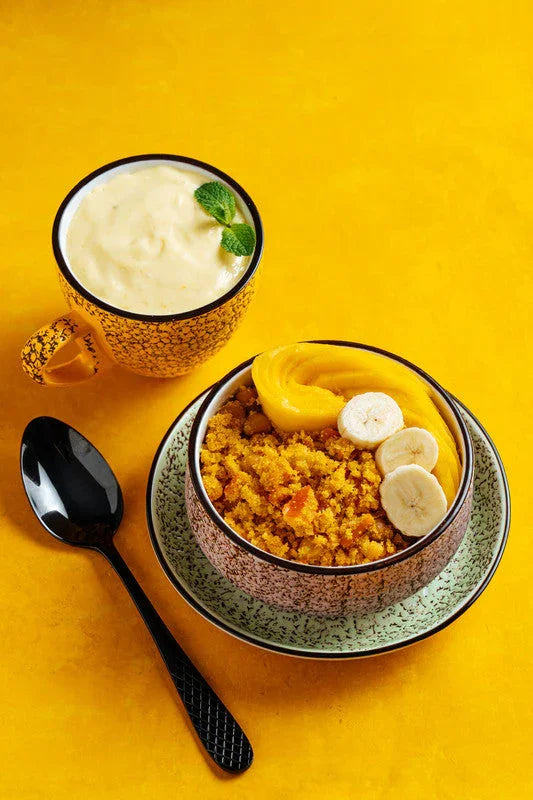 Artisan breakfast bowl with crumble, sliced bananas, and mango beside a creamy drink, on bright yellow background