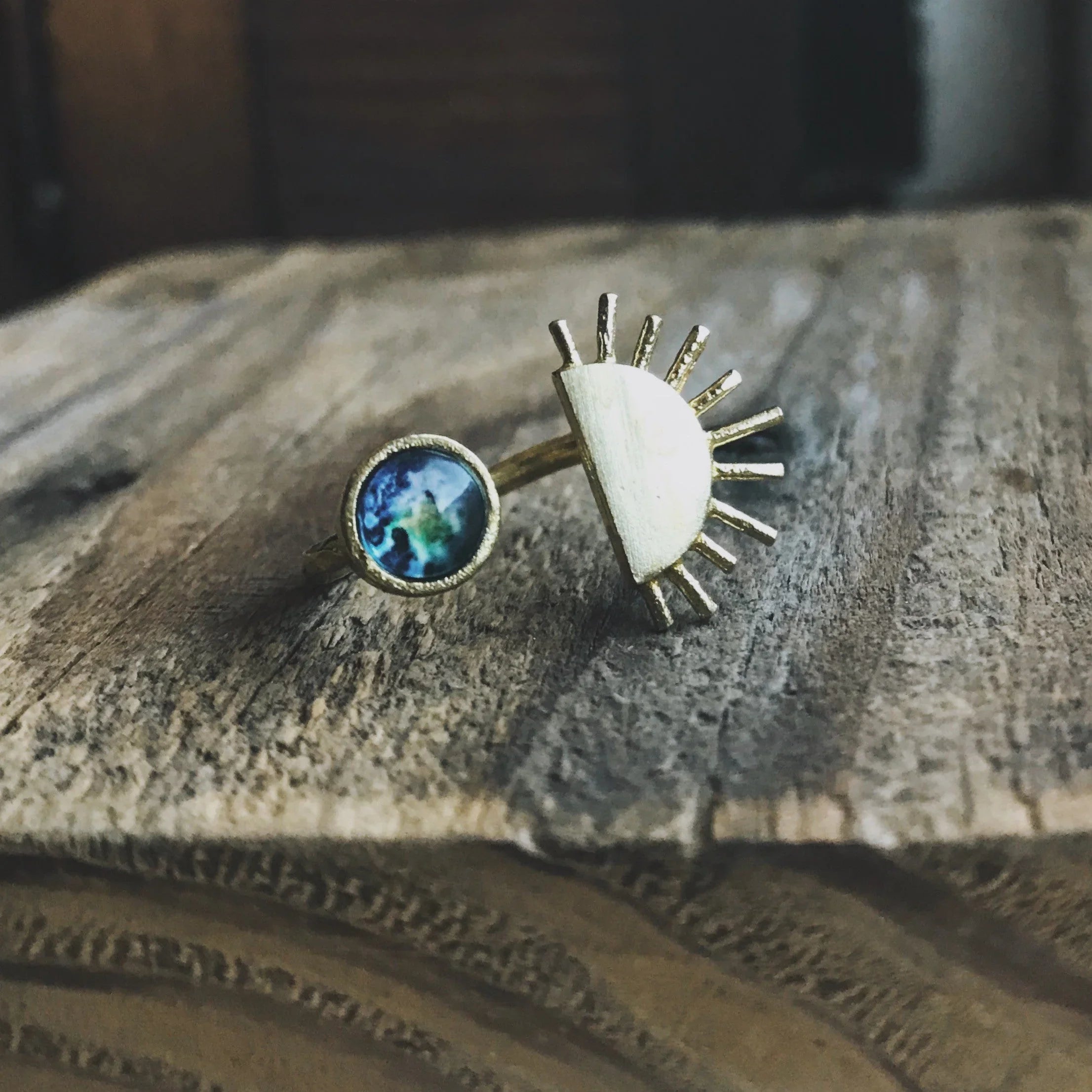Gold artistic ring with cosmic Earth design and sunburst accent on rustic wood, Qu!rk Boutique