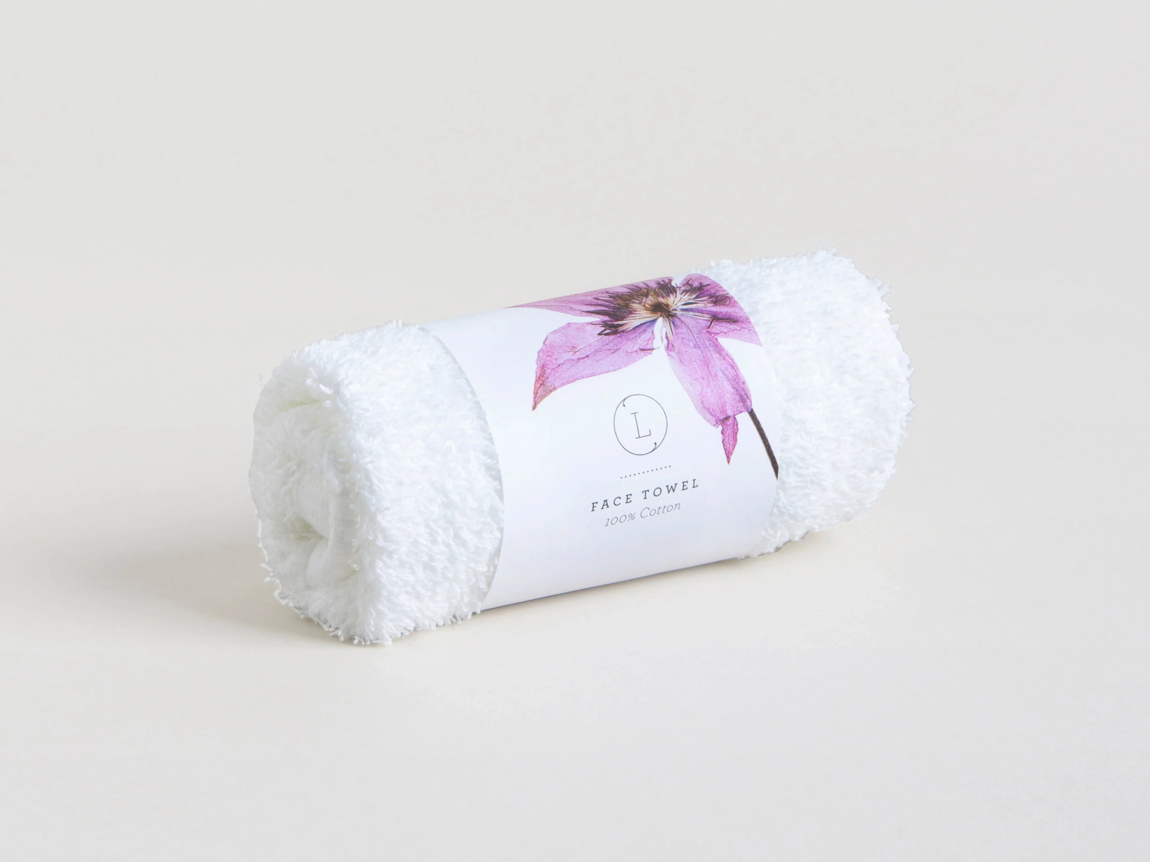 Rolled white face towel wrapped with a label featuring a purple flower and cotton text