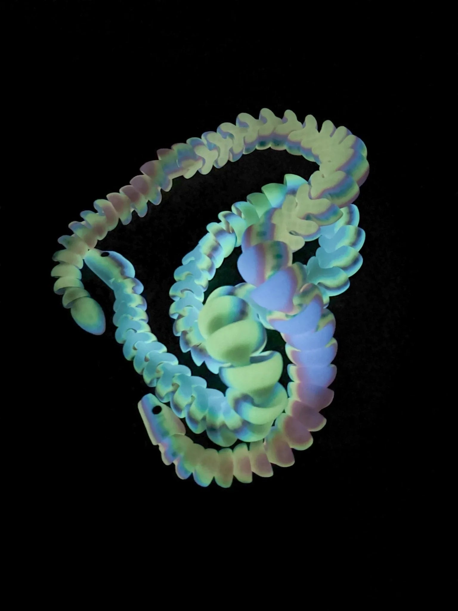 Glow-in-the-dark rainbow articulated snake 3D printed fidget toy on black background
