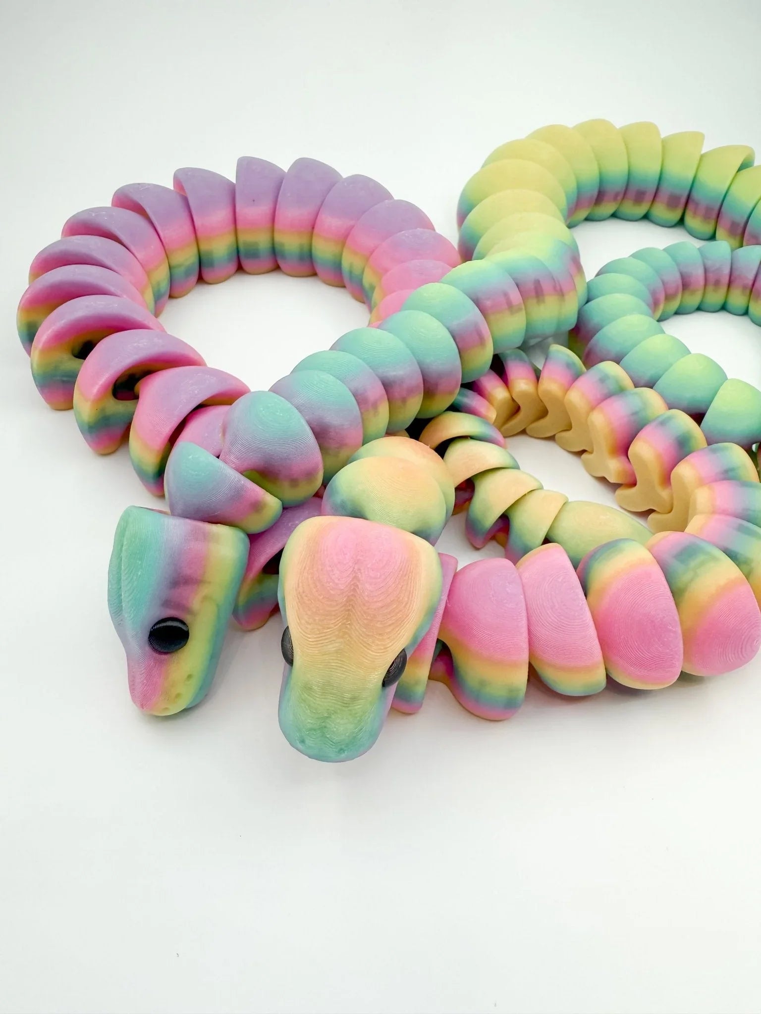 3D printed articulated rainbow snake fidget toys in pastel colors on white background