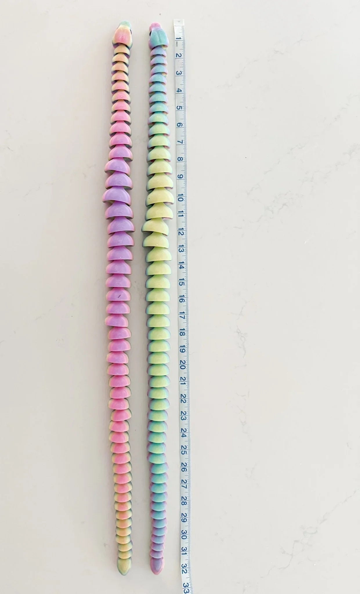Two 32-inch rainbow 3D printed articulated snake fidget toys beside a measuring tape on white.