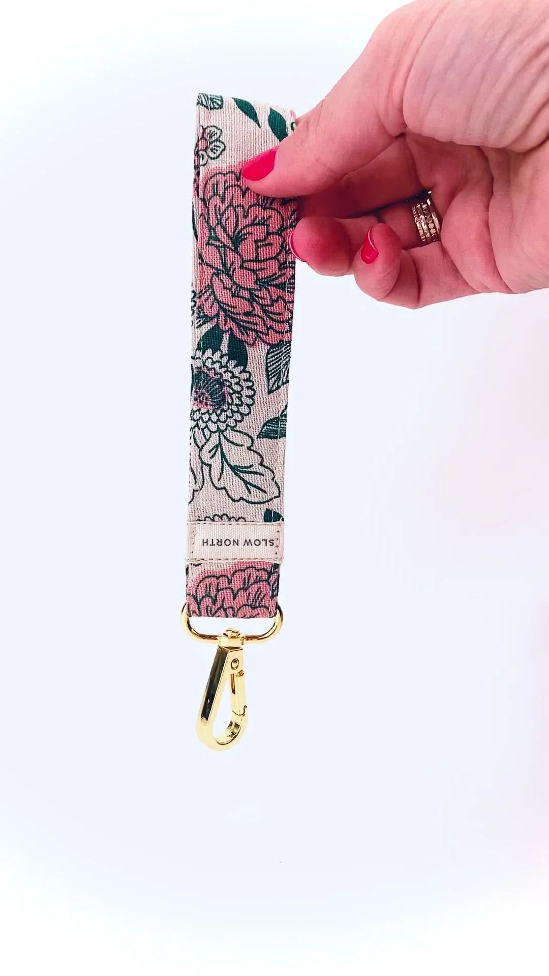 Hand holding floral fabric keychain wristlet with gold clasp and Slow North label