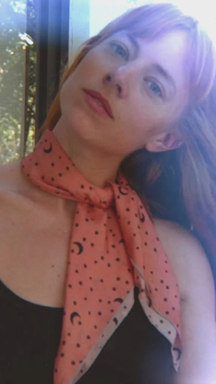 Close-up portrait of woman wearing coral scarf with crescent moon and dots, soft natural light