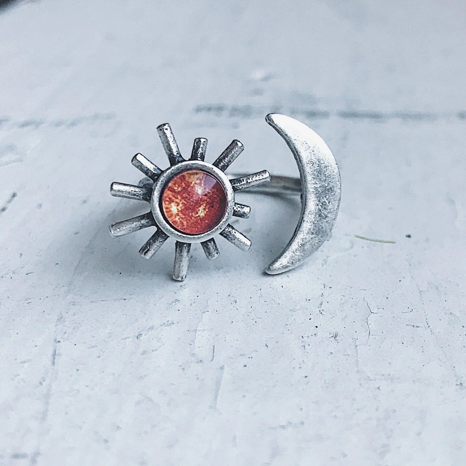 Silver ring with sun design featuring a red stone and adjacent crescent moon on white surface