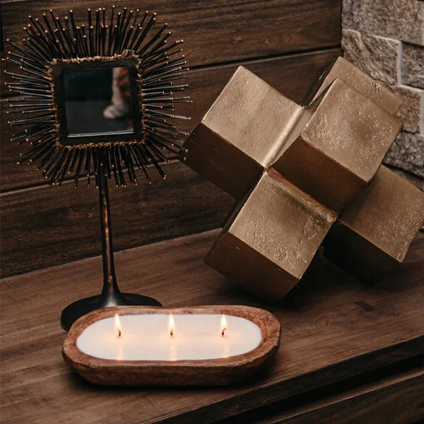 Three wick dough bowl candle, gold geometric sculpture, and starburst mirror on wood table