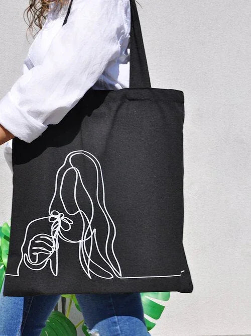 Black tote bag with white continuous line art of woman holding flower, worn by person in white shirt and jeans