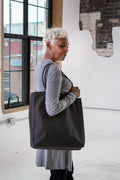 Mature woman in gray outfit carrying large black tote bag in bright industrial loft space