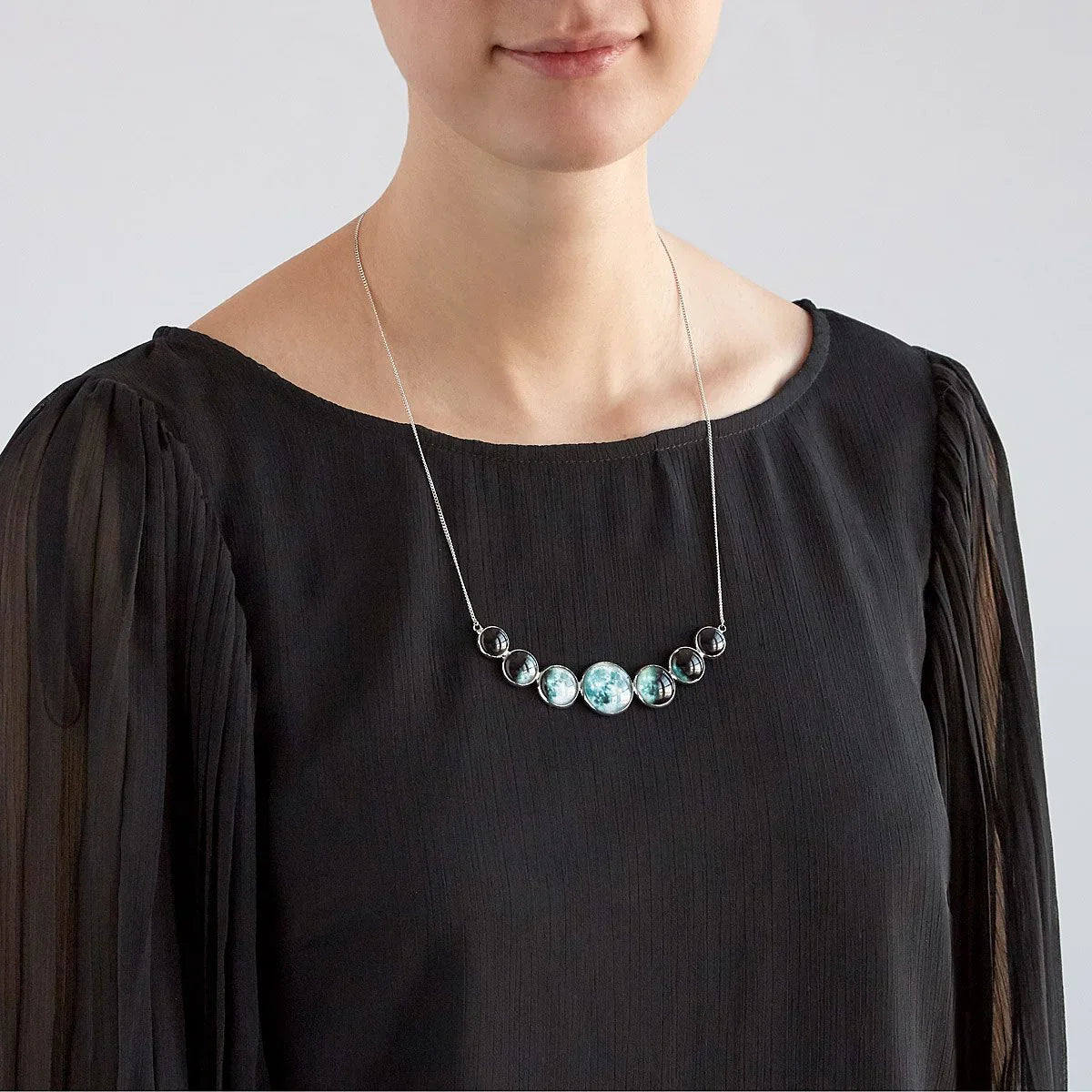 Woman wearing black blouse with pleated sleeves and celestial moon phase necklace