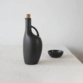 Minimalist black ceramic bottle with cork and matching bowl on white table, Qu!rk Boutique