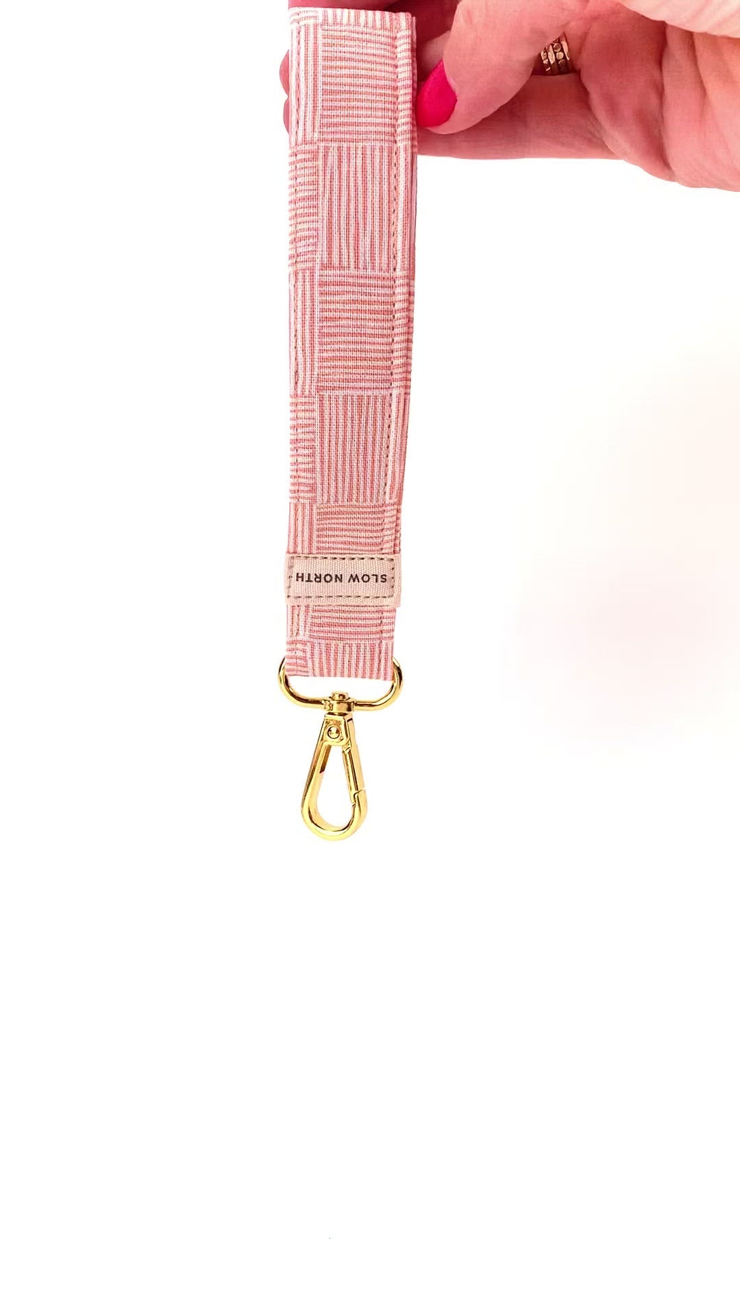 Hand holding pink patterned fabric keychain with gold clasp and Slow North label