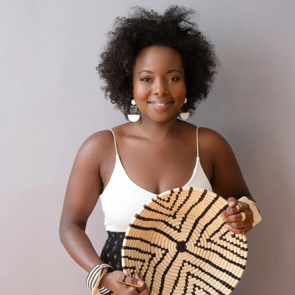 Woman with natural hair holding woven artisan basket, wearing bold jewelry at Qu!rk Boutique