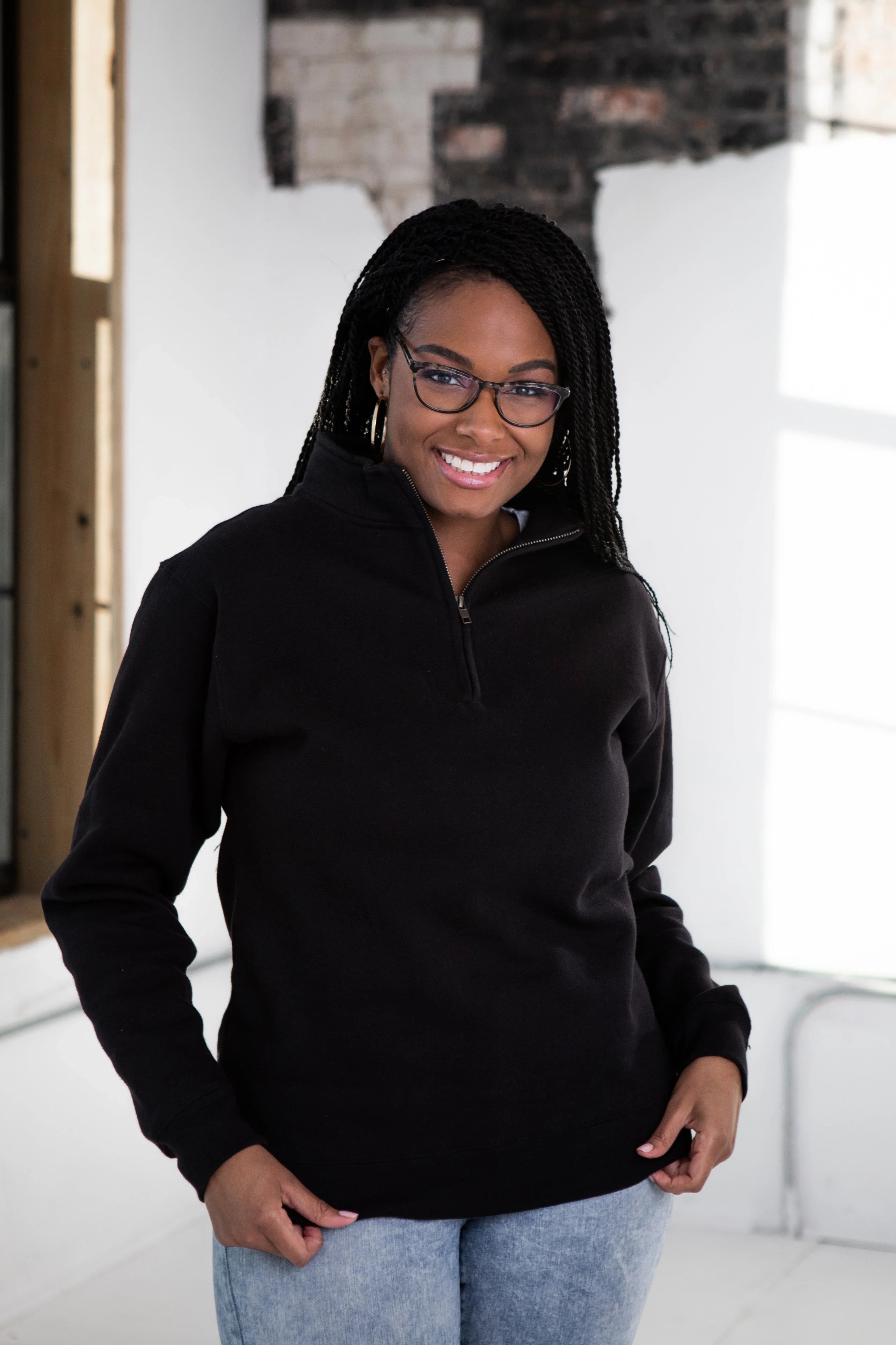 Woman wearing black quarter-zip pullover and glasses, smiling, at Qu!rk Boutique.