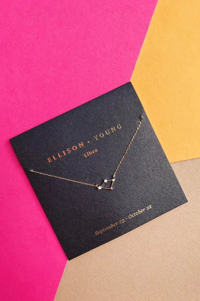 Ellison + Young Libra constellation gold necklace displayed on black card with pink, yellow, and beige background