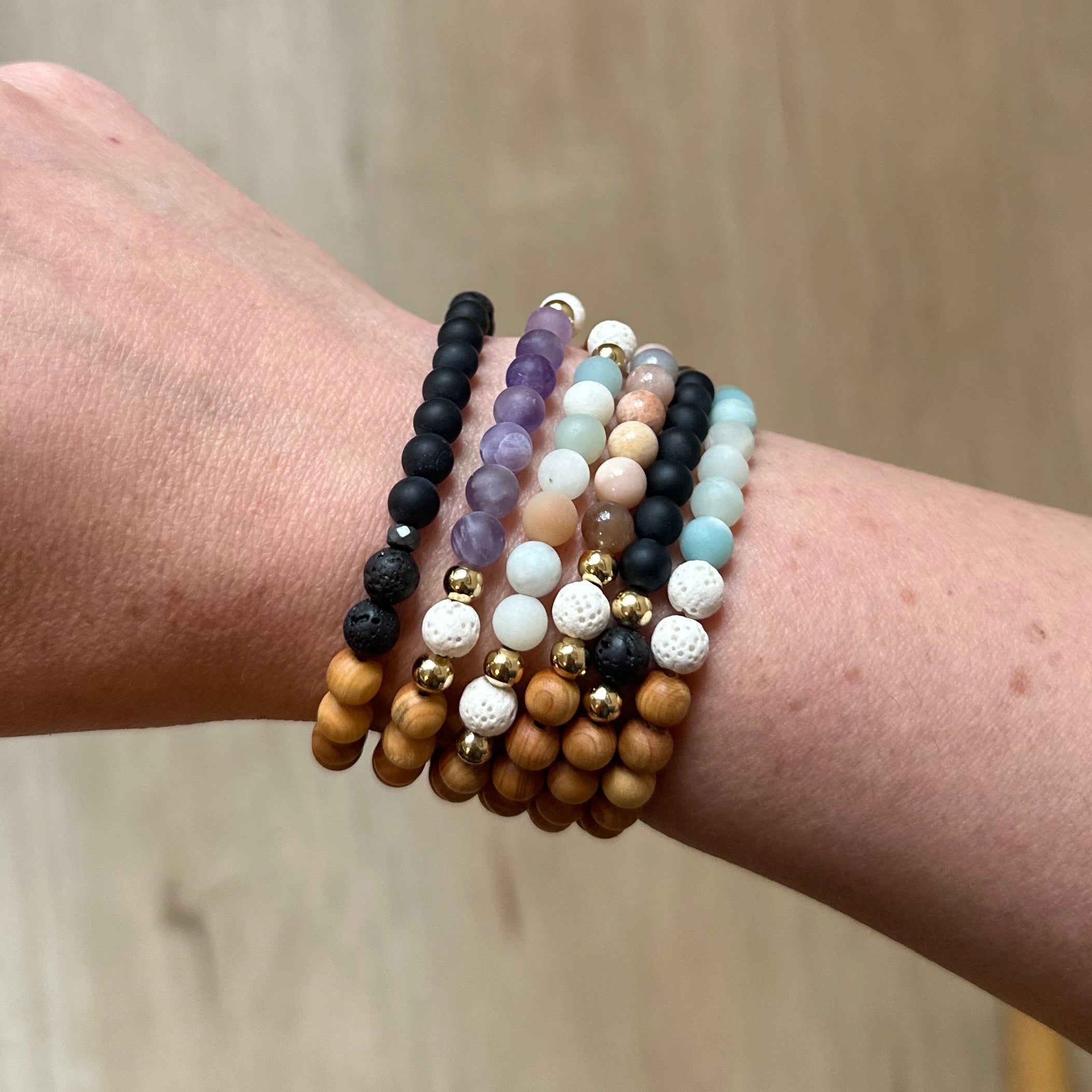 Wrist wearing multiple beaded bracelets with black, purple, white, pastel, wooden, and gold beads