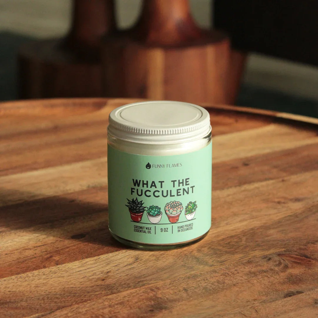 9 oz coconut wax essential oil candle labeled What The Fucculent with succulent illustrations on wooden table