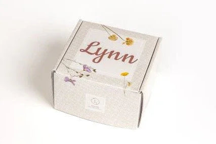Small white cardboard box with the name Lynn and floral design on a white background
