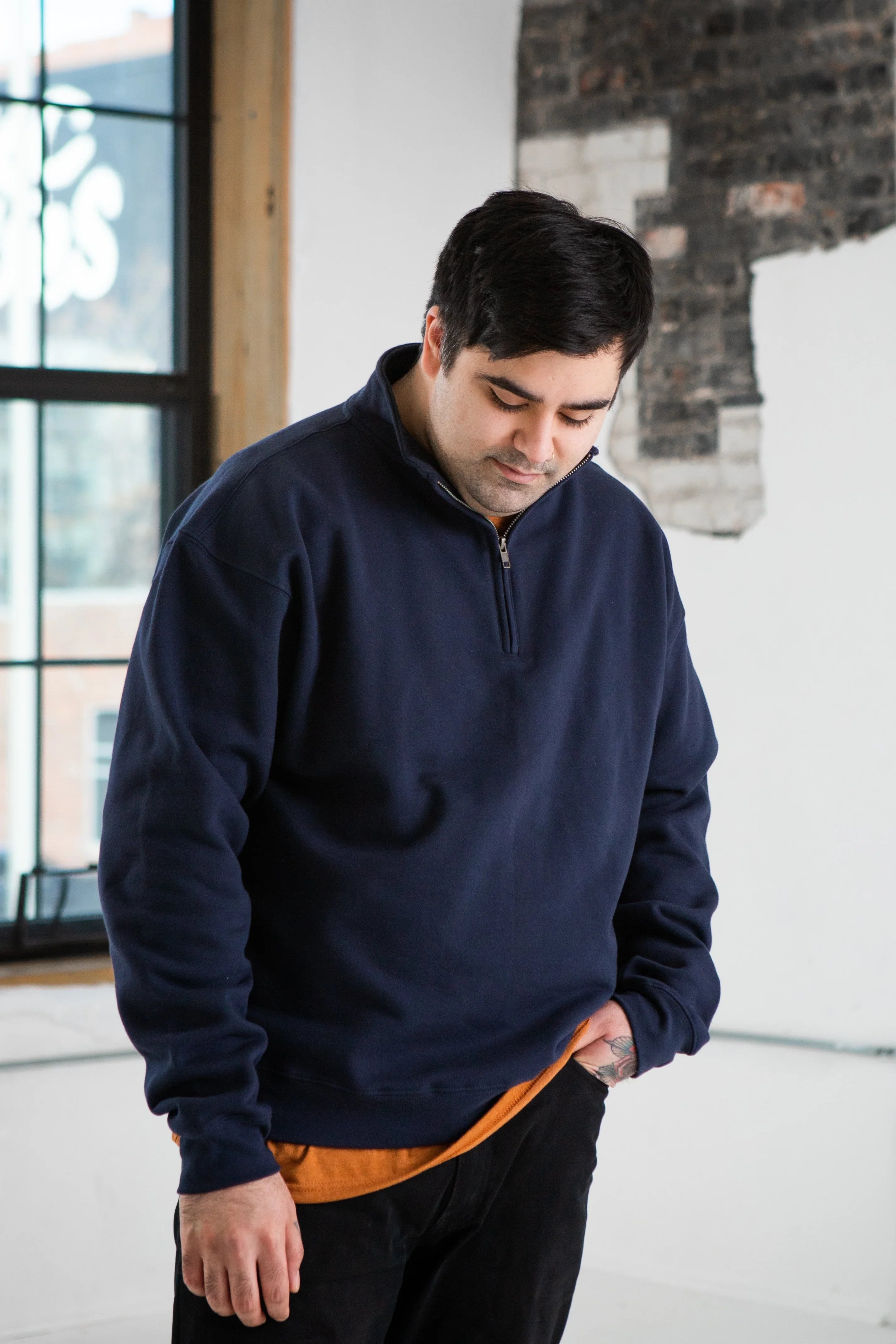 Man in navy quarter-zip pullover by window, modern urban setting, Qu!rk Boutique style