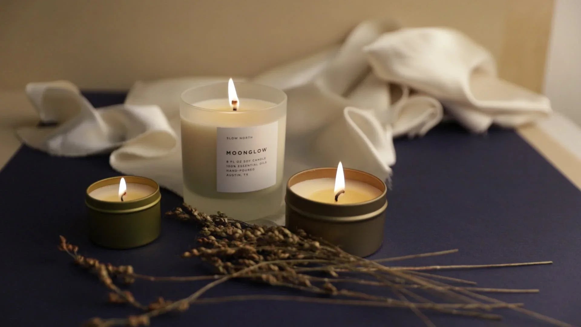 Three lit soy candles with dried botanicals and white cloth, Qu!rk Boutique gift shop style
