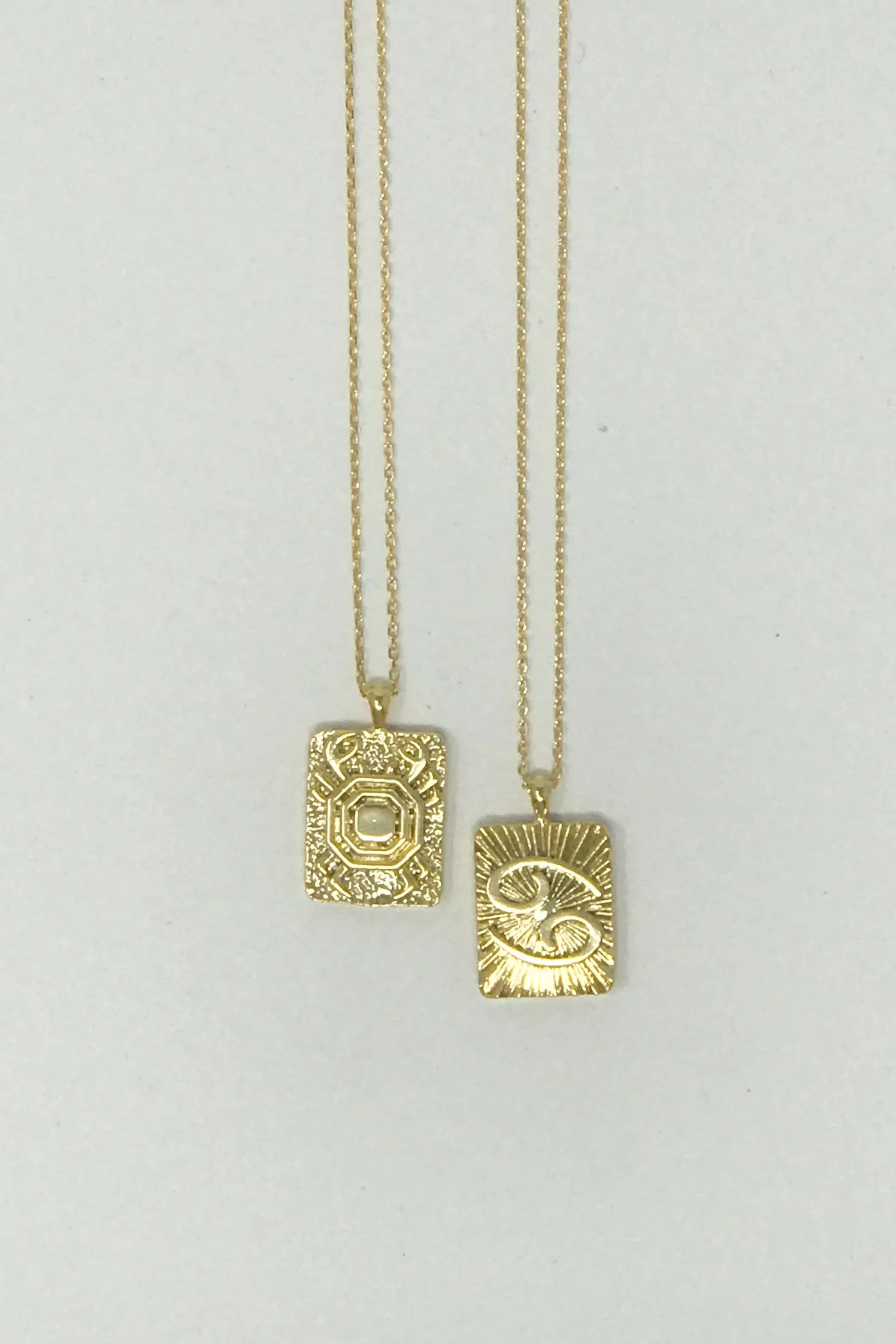 Two gold rectangular pendant necklaces with intricate textured designs on white background