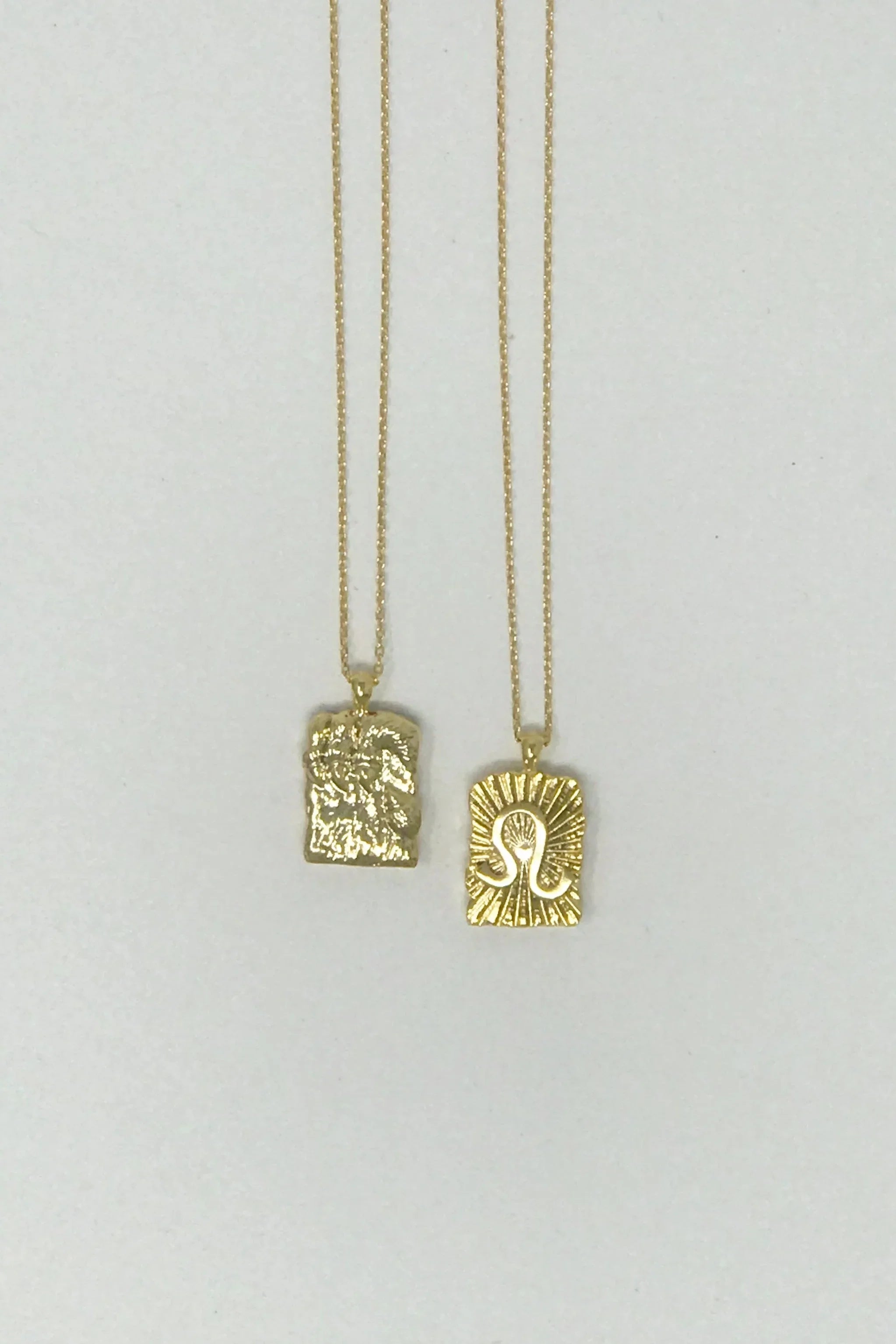 Two gold pendant necklaces with textured rectangular charms on delicate chains