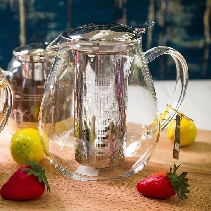Clear glass teapot with metal infuser on wooden board, surrounded by strawberries and lemons