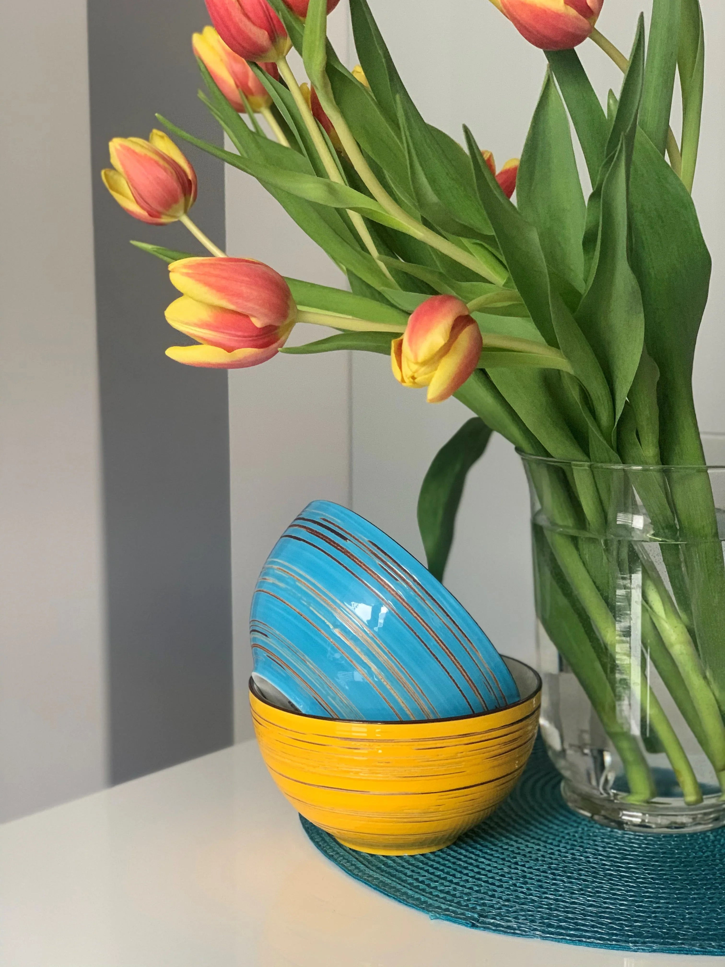 Colorful ceramic bowls with orange tulips in a clear vase on a modern table at Qu!rk Boutique.