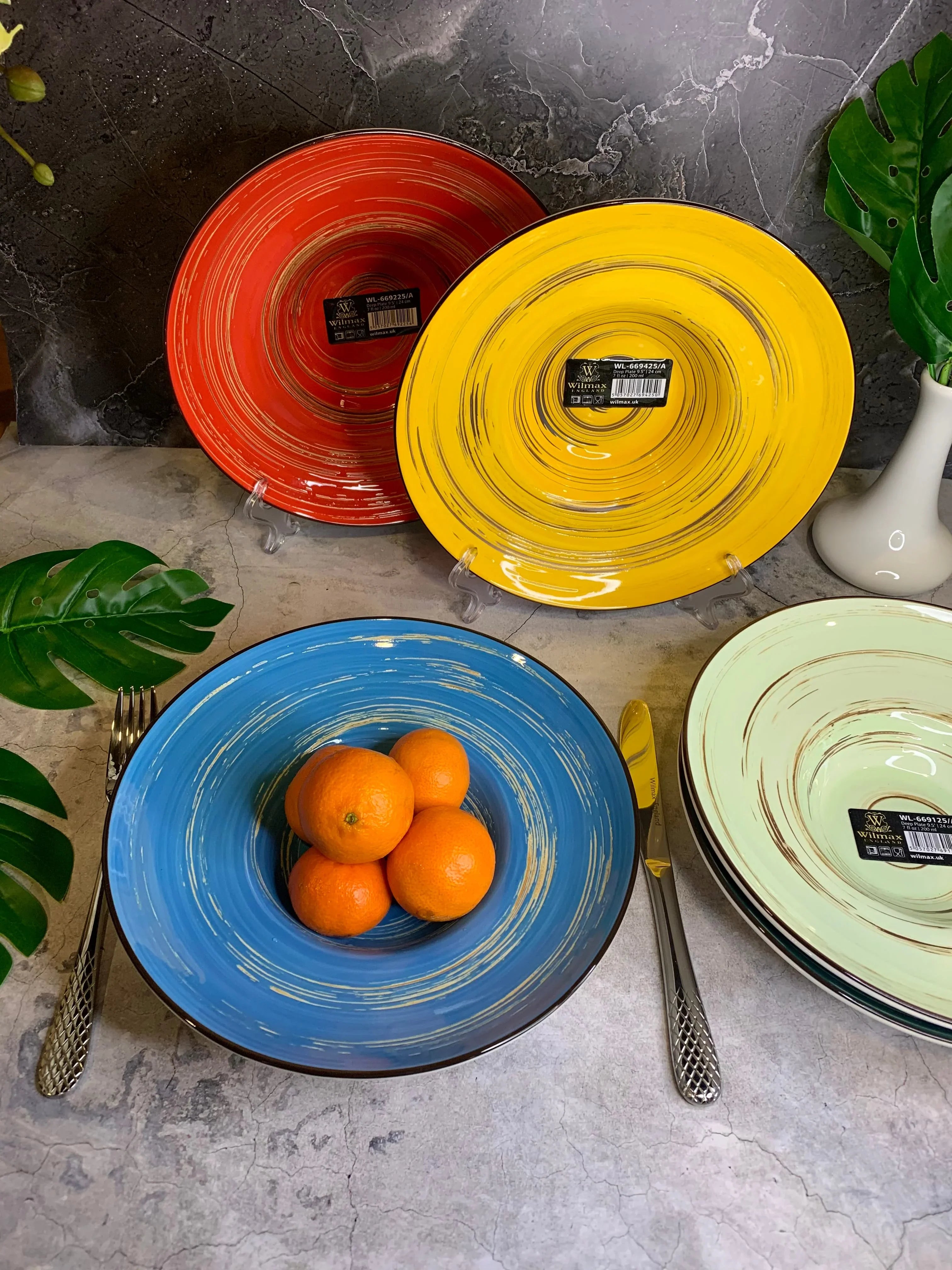 Colorful artist-designed swirl plates with oranges, styled on a stone surface at Qu!rk Boutique