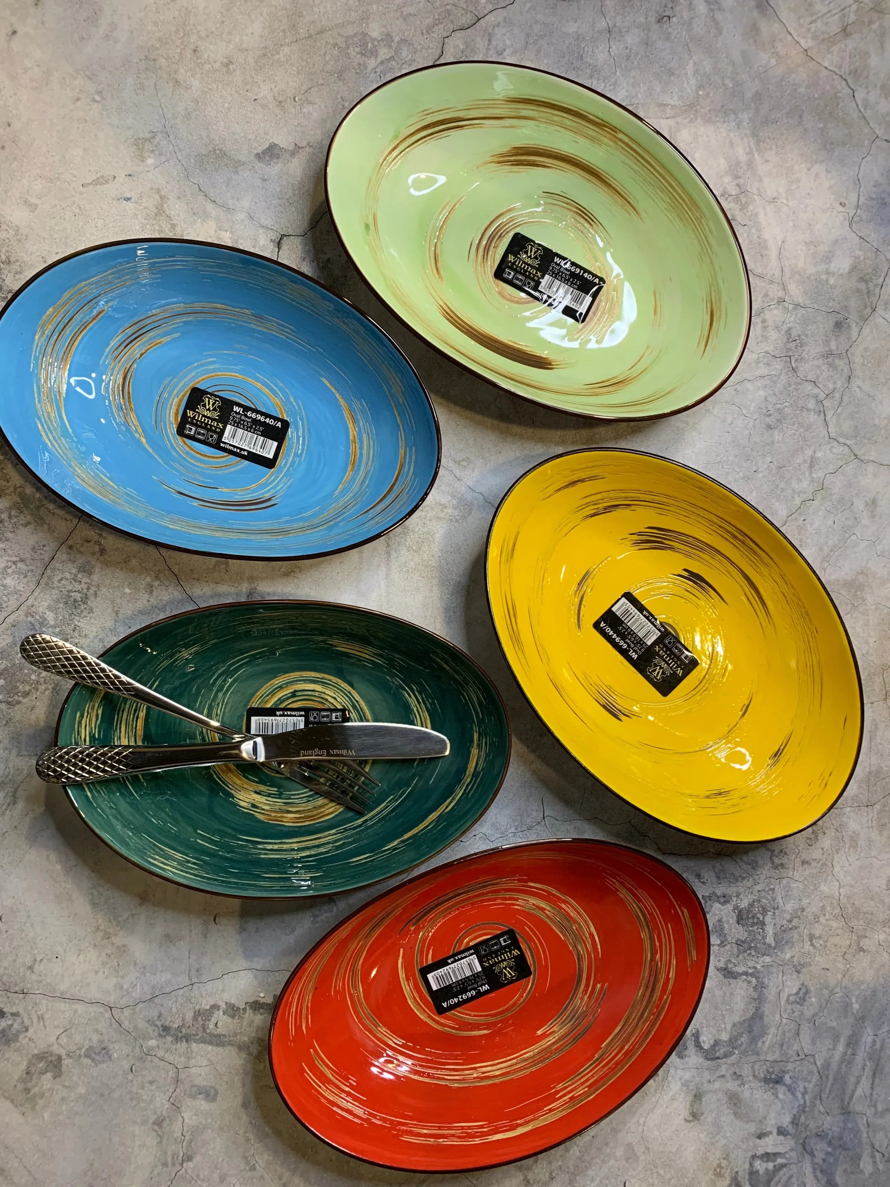 Colorful oval ceramic bowls with swirl designs from Qu!rk Boutique, green bowl with cutlery.