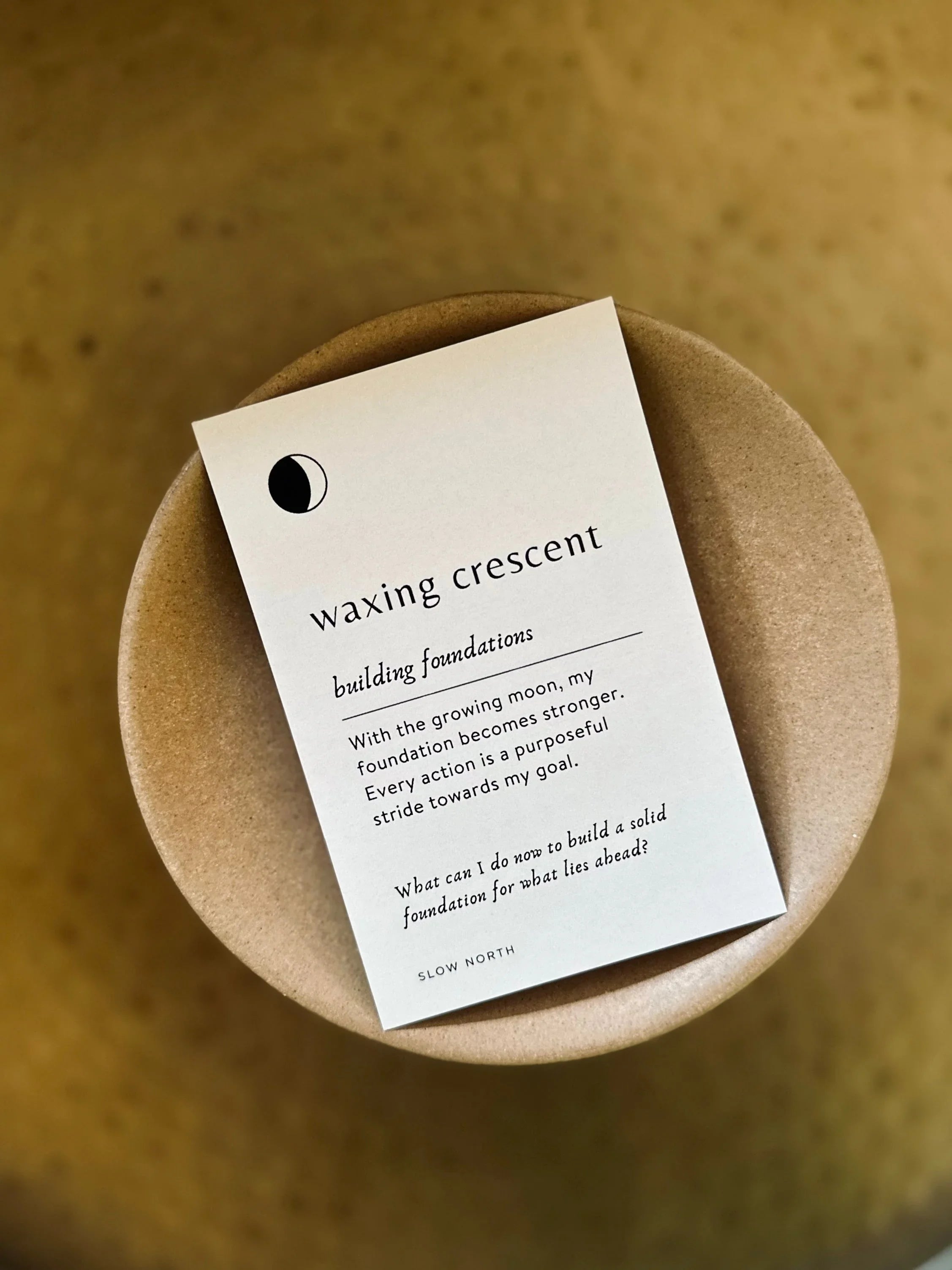 Waxing crescent card with motivational text on building foundations, placed on a round brown surface