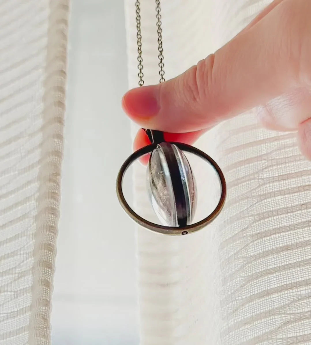 Hand holding a cosmic pendant necklace with glass orb, Qu!rk Boutique artist-designed jewelry