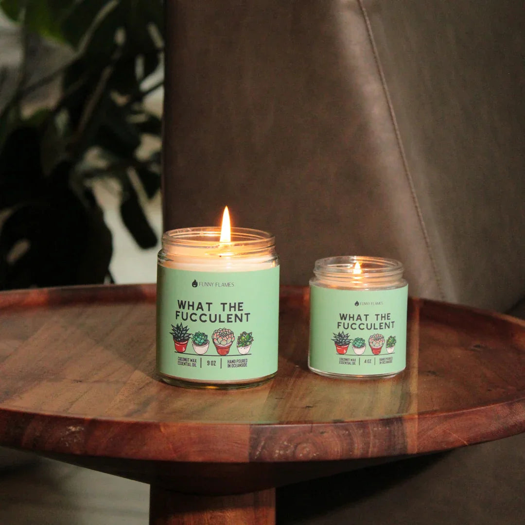 Two lit What The Fucculent scented candles with succulent plant illustrations on a wooden tray
