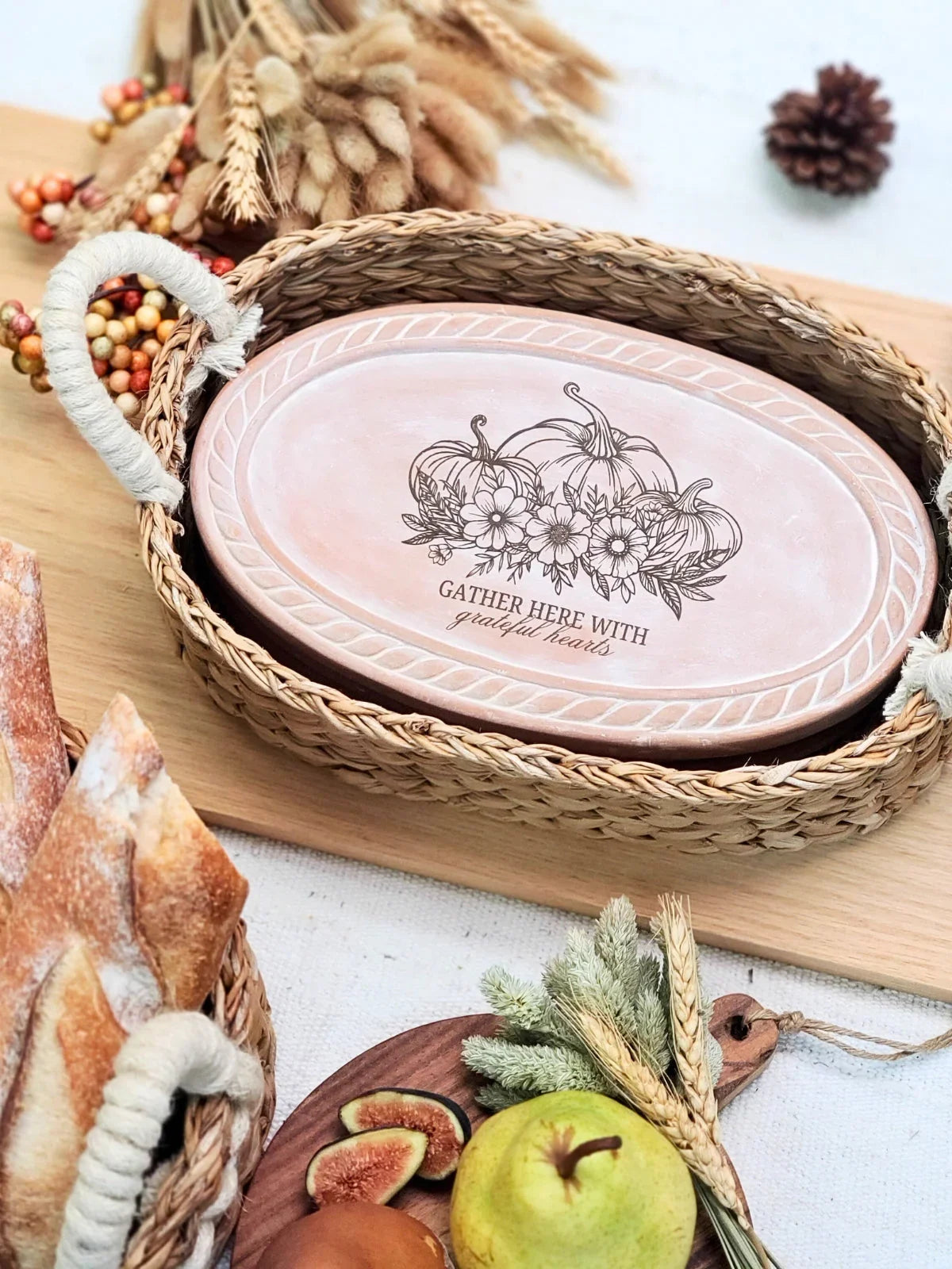 Oval pink ceramic serving dish with pumpkins and floral design in woven basket on wooden board