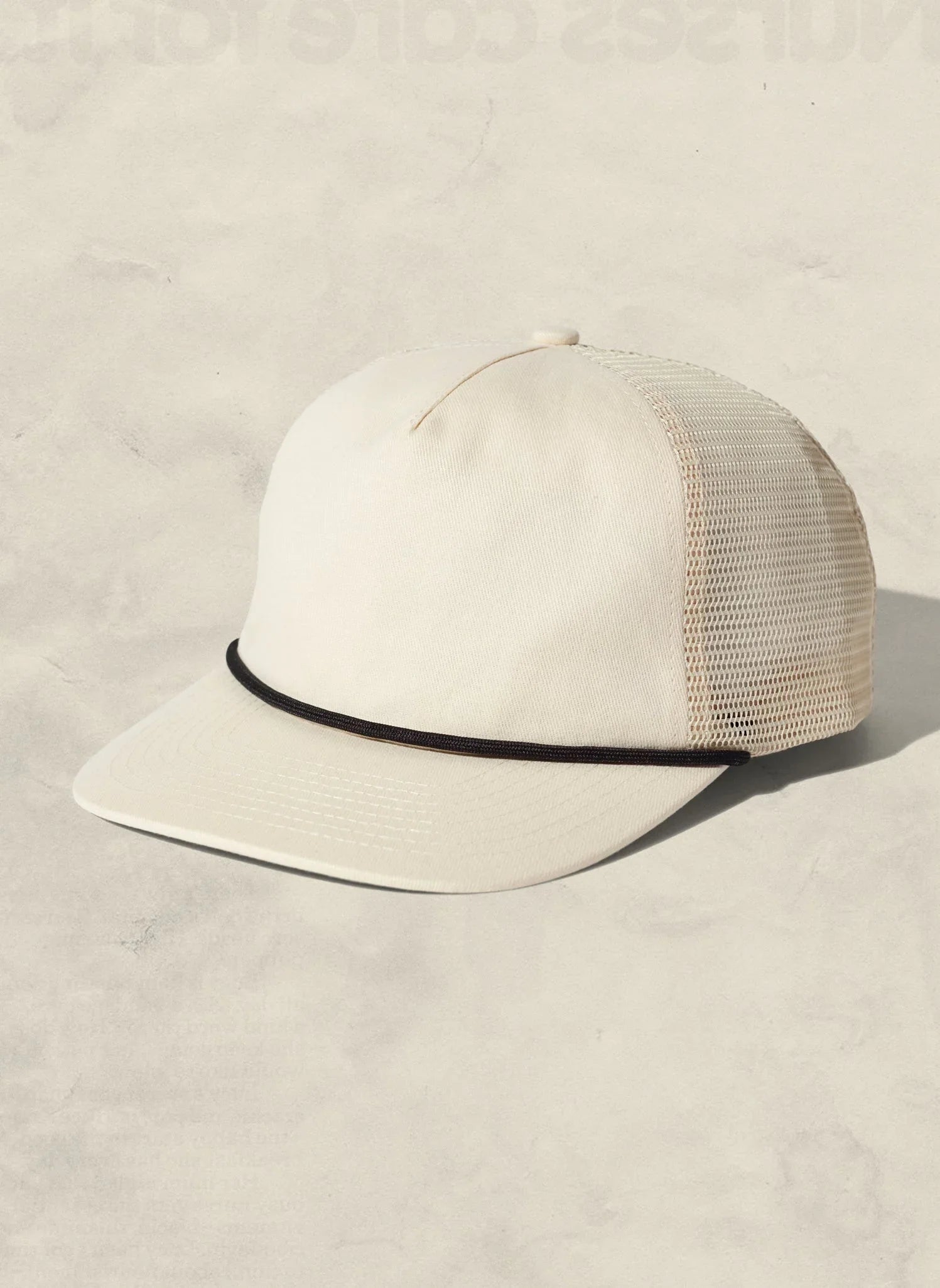 Cream mesh trucker hat with black cord detail, showcased on neutral background at Qu!rk Boutique