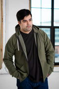 Man in olive hoodie and black t-shirt from Qu!rk Boutique, standing by window, casual style