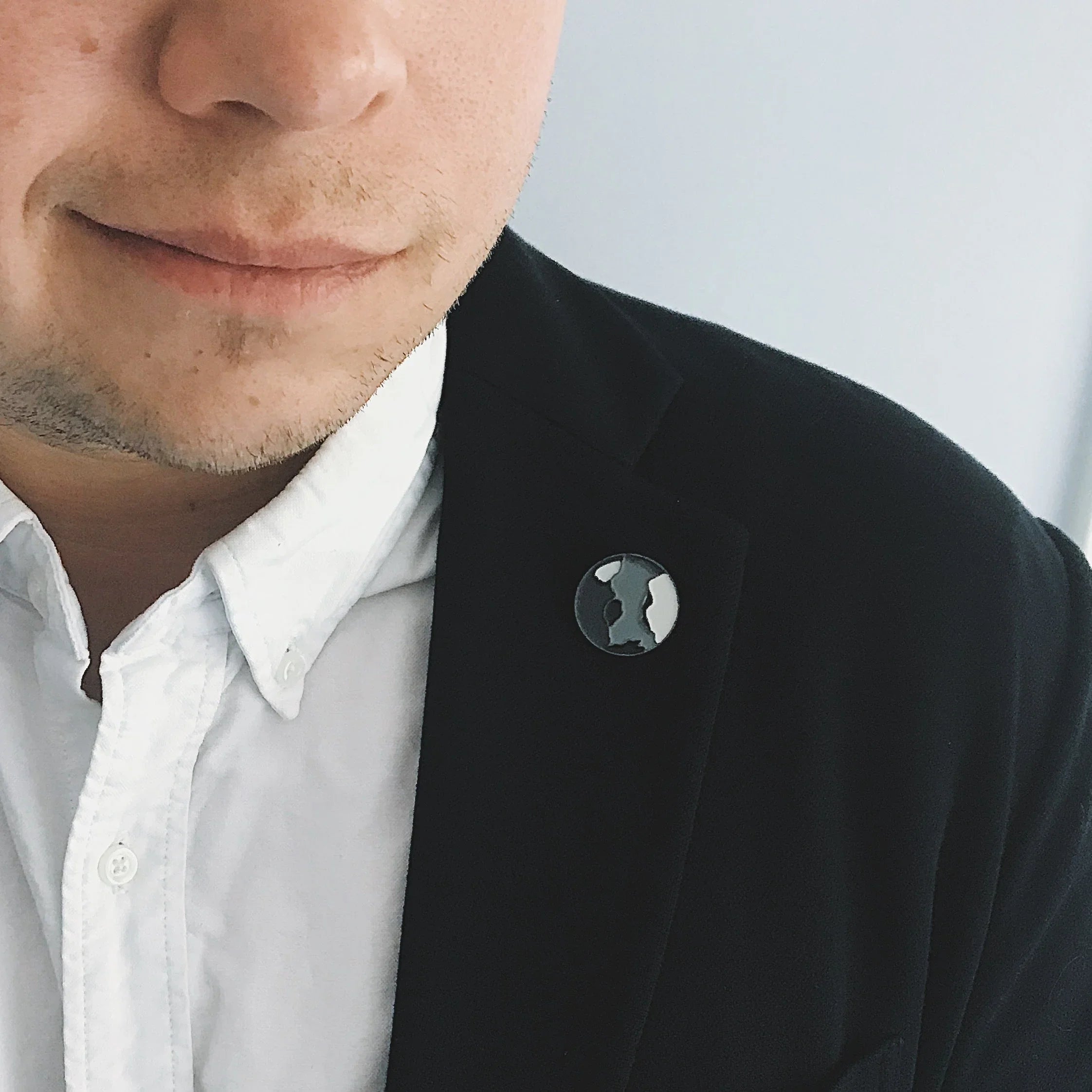 Close-up of a man wearing a black blazer with a black-and-white face silhouette pin on the lapel