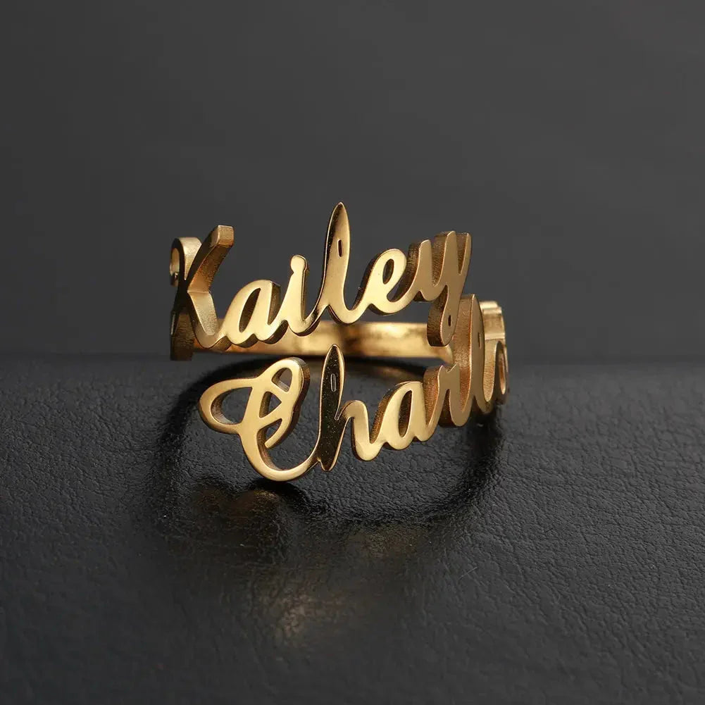 Gold personalized name ring with the names Kailey and Charlie on black textured surface