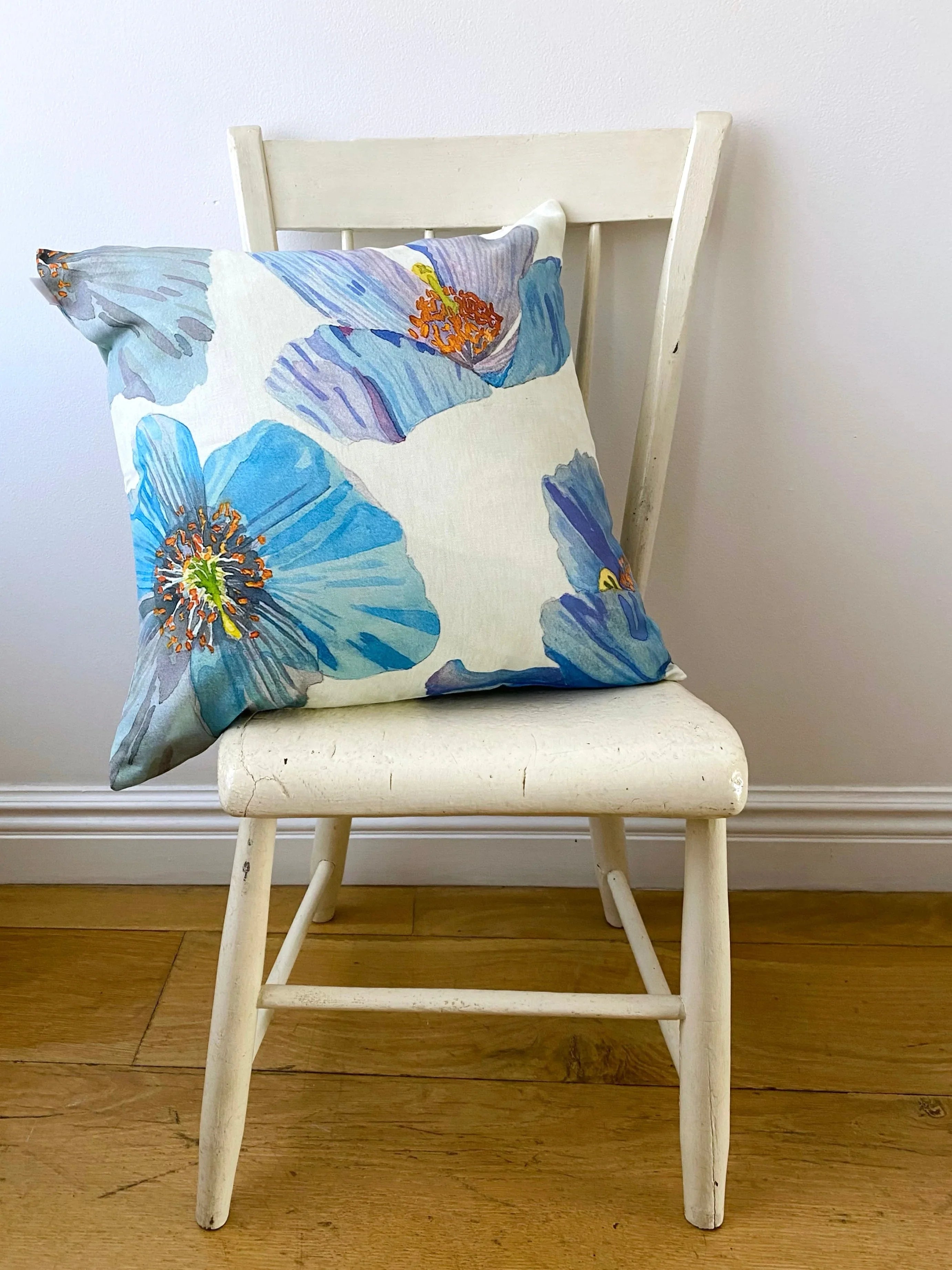 White wooden chair with a decorative pillow featuring large blue floral prints on a wooden floor
