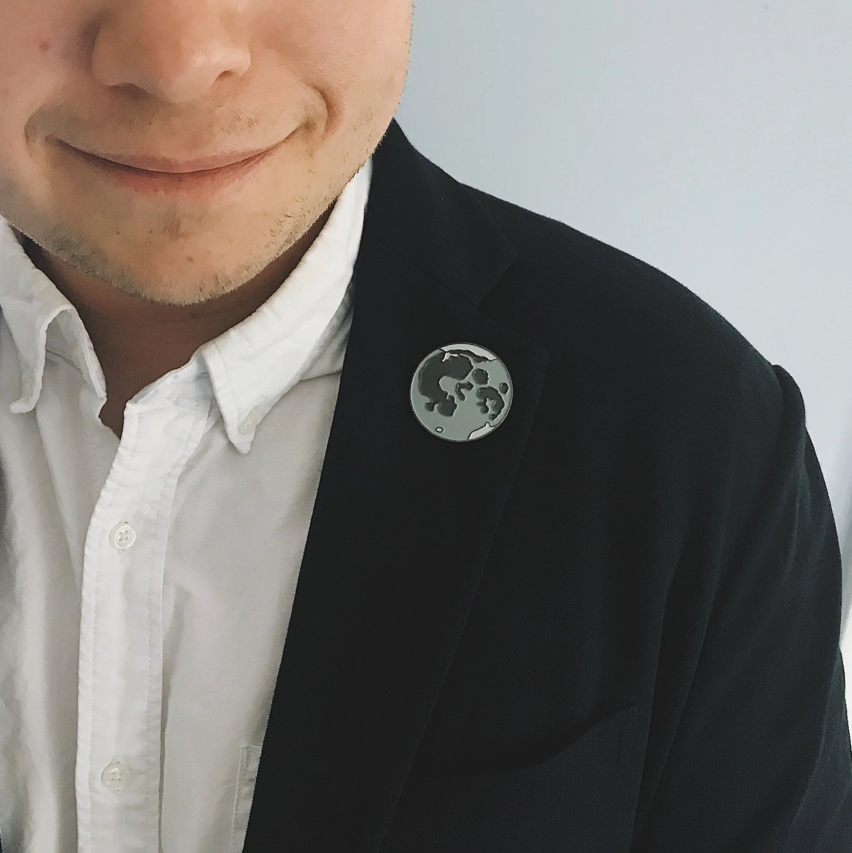 Man wearing white shirt and dark blazer with a moon crater design lapel pin
