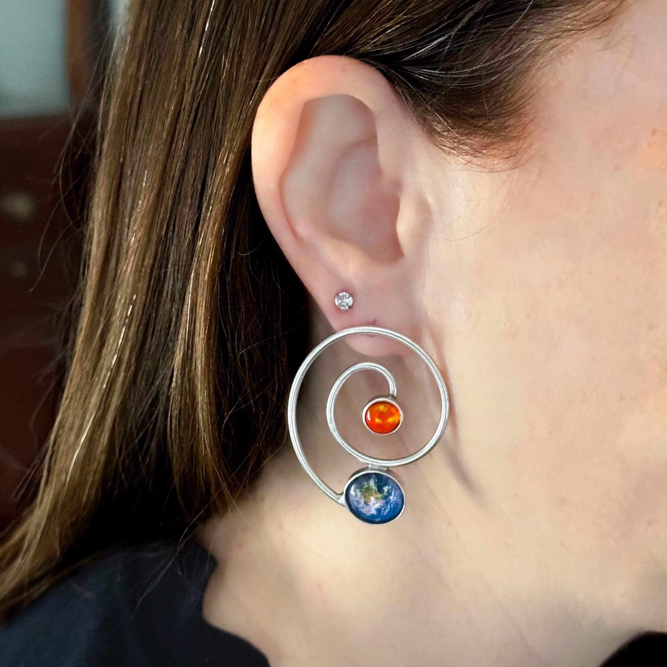 Spiral silver earring with planet and sun design worn by woman, cosmic jewelry at Qu!rk Boutique