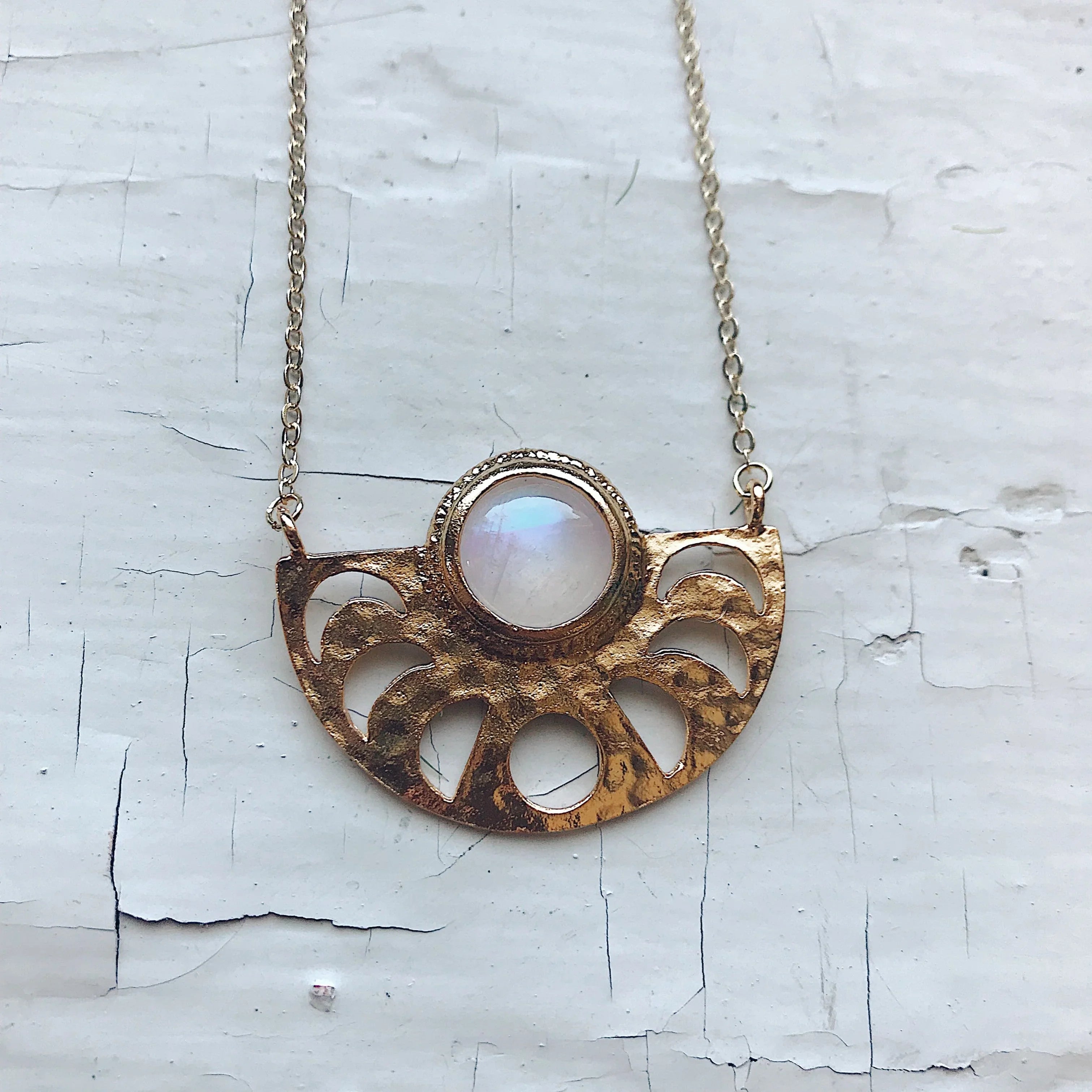 Gold pendant necklace with semi-circle cutout design and central round moonstone on white textured surface