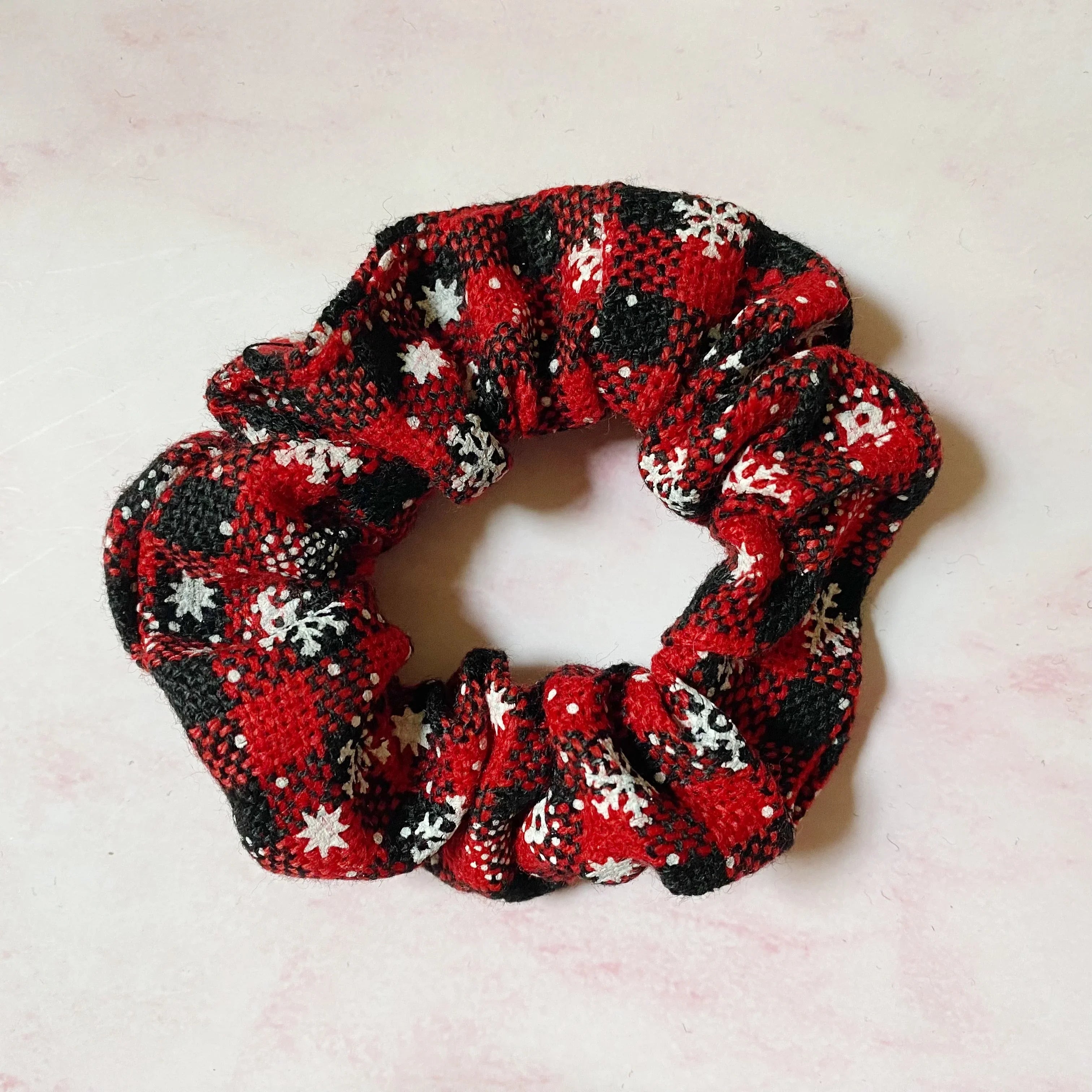 Red and black plaid fabric scrunchie with white snowflake patterns on light pink background