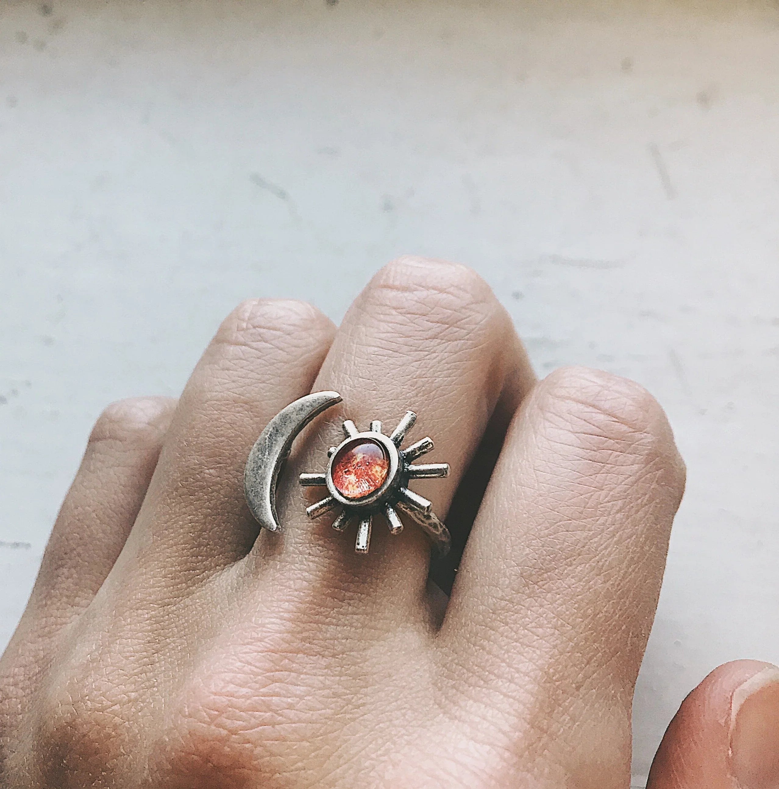 Silver sun and crescent moon rings on a hand with a light background