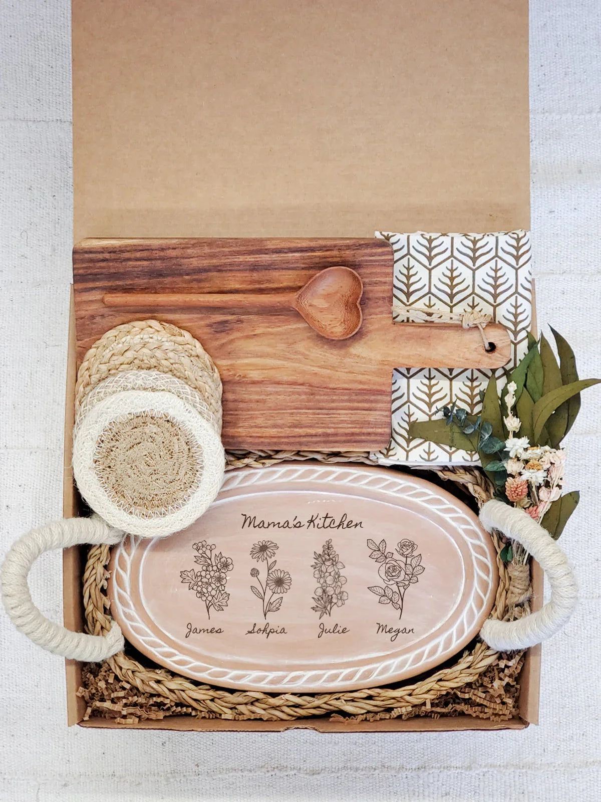 Gift box with personalized ceramic platter reading Mama's Kitchen, wooden heart spoon, coasters, and cloth napkin