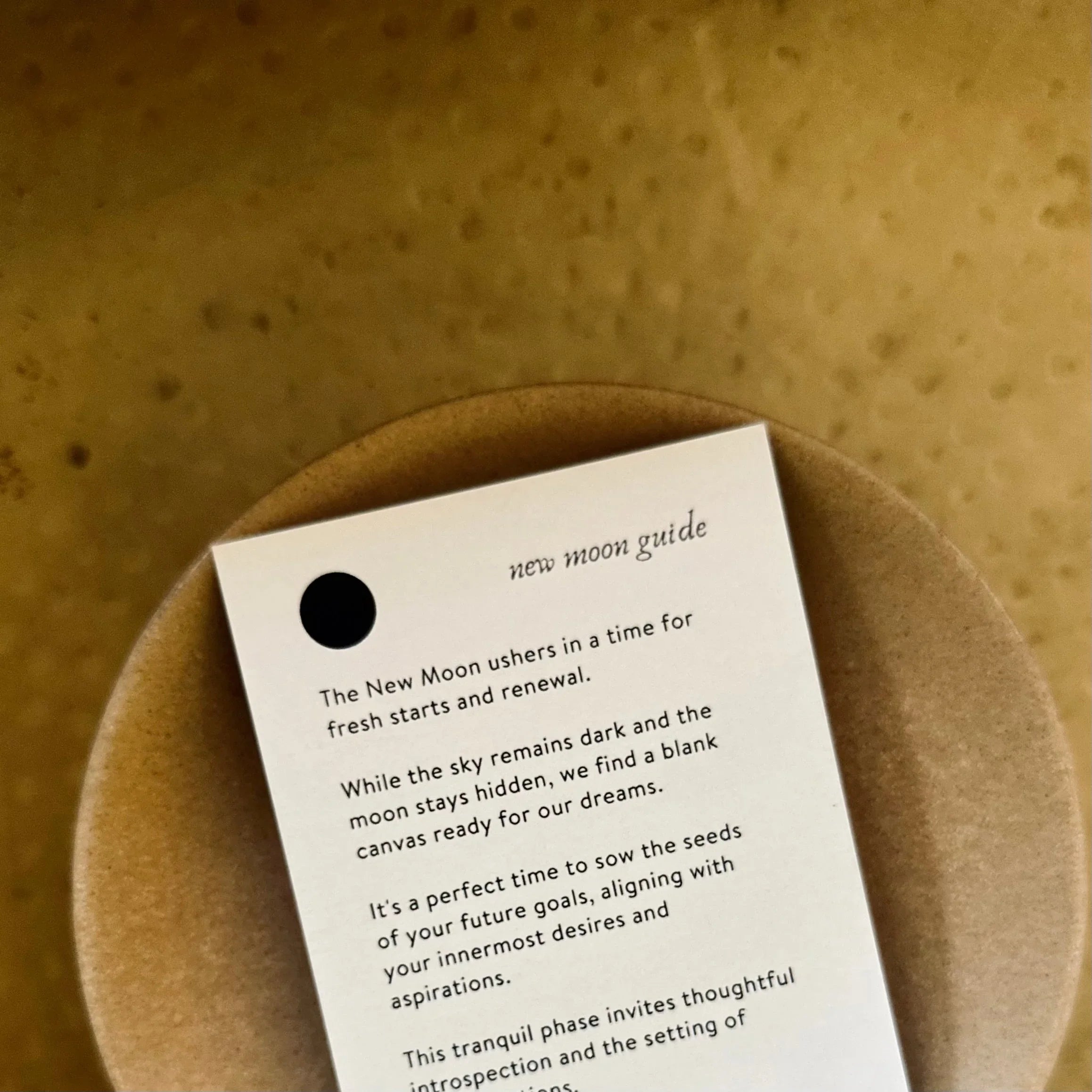 New moon guide card with text about fresh starts and renewal on brown ceramic plate
