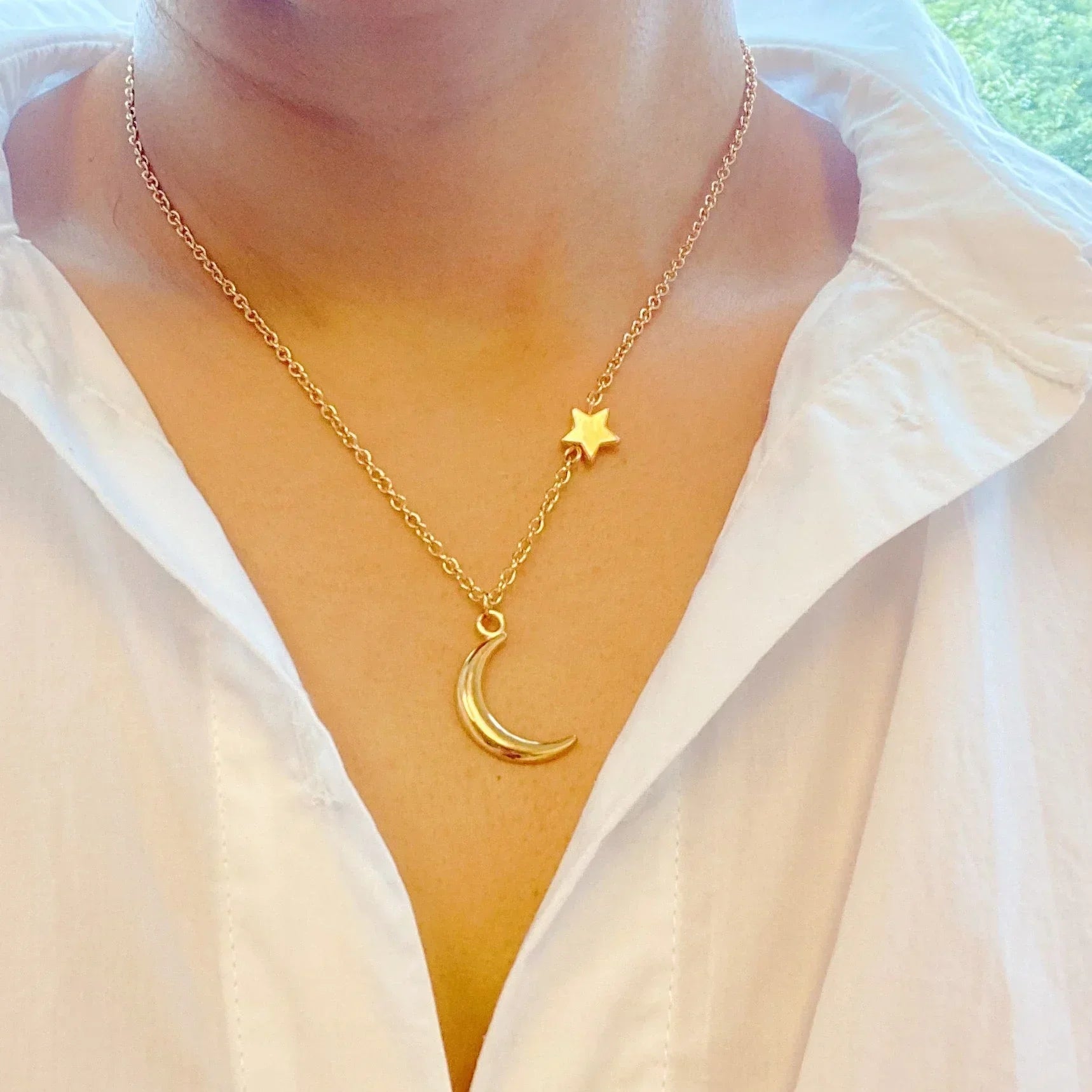 Gold necklace with crescent moon and star pendants worn with white shirt collar