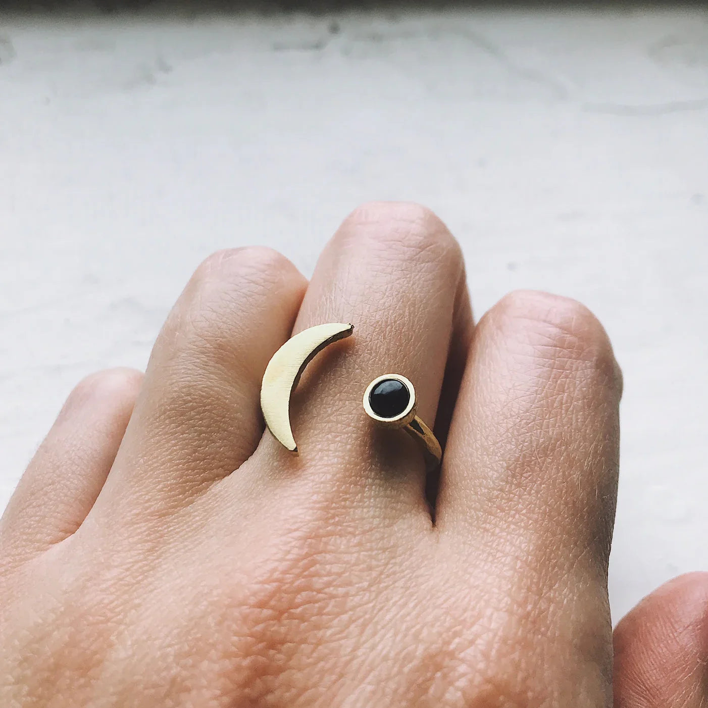 Hand wearing open gold ring with crescent moon and black stone accents on fingers