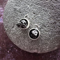 Silver dangle earrings with irregular black stones, displayed on textured gray stone surface