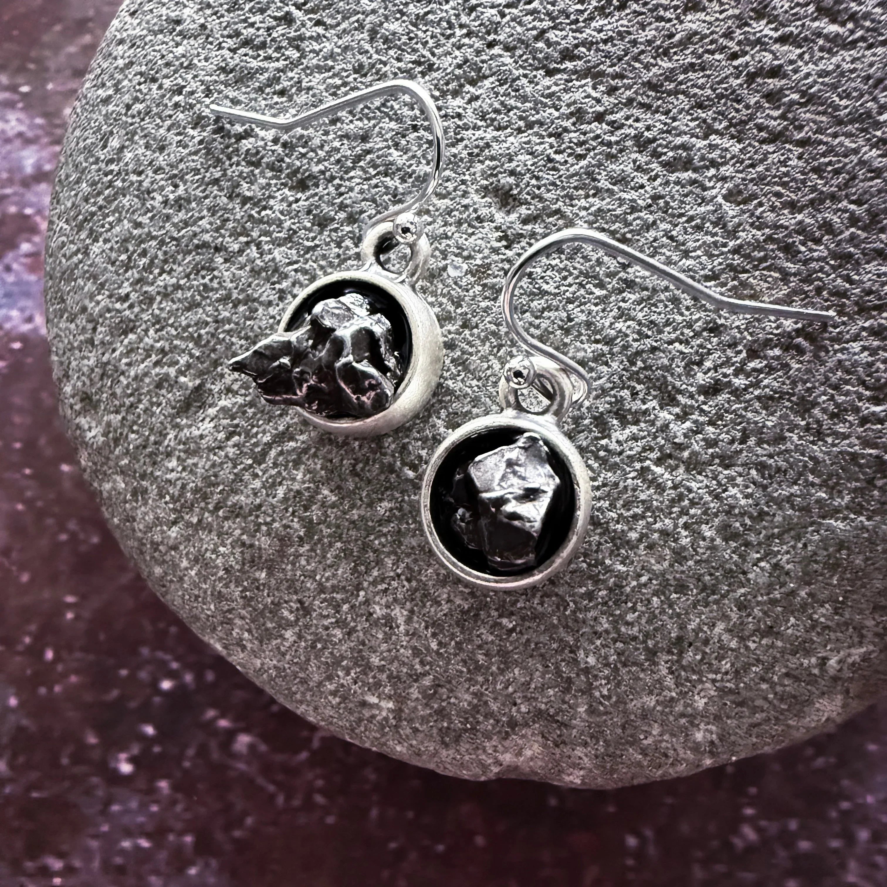 Silver dangle earrings with irregular black stones, displayed on textured gray stone surface