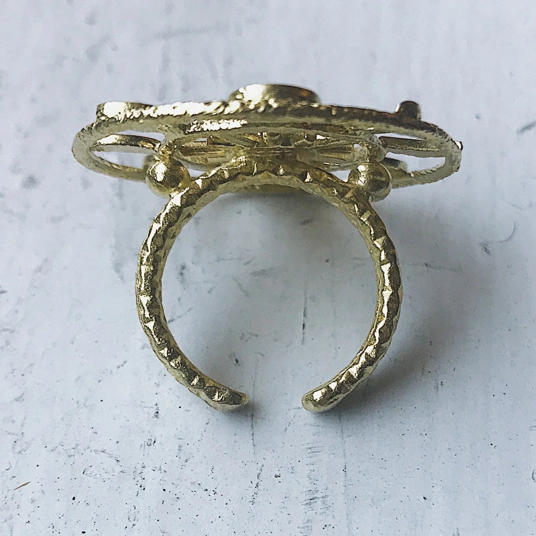 Close-up of an open adjustable textured gold metal ring on a white surface